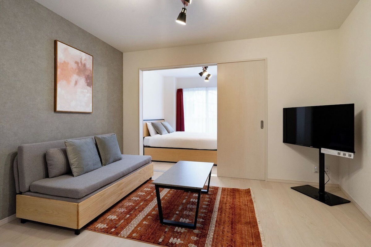 Quarto moderno com sofá, televisão, cama e vista para outro ambiente.