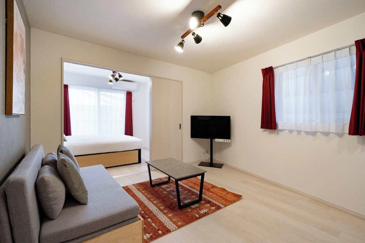 Quarto de hotel moderno com cama, sofá, televisão e janela com cortinas.