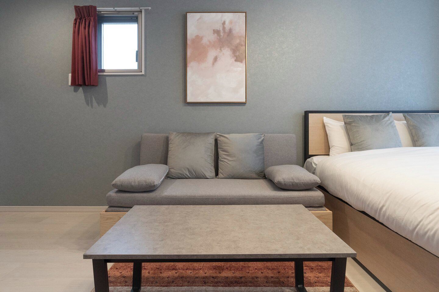 Een slaapkamer met een bed, een bank, een tafel en een raam met gordijnen.