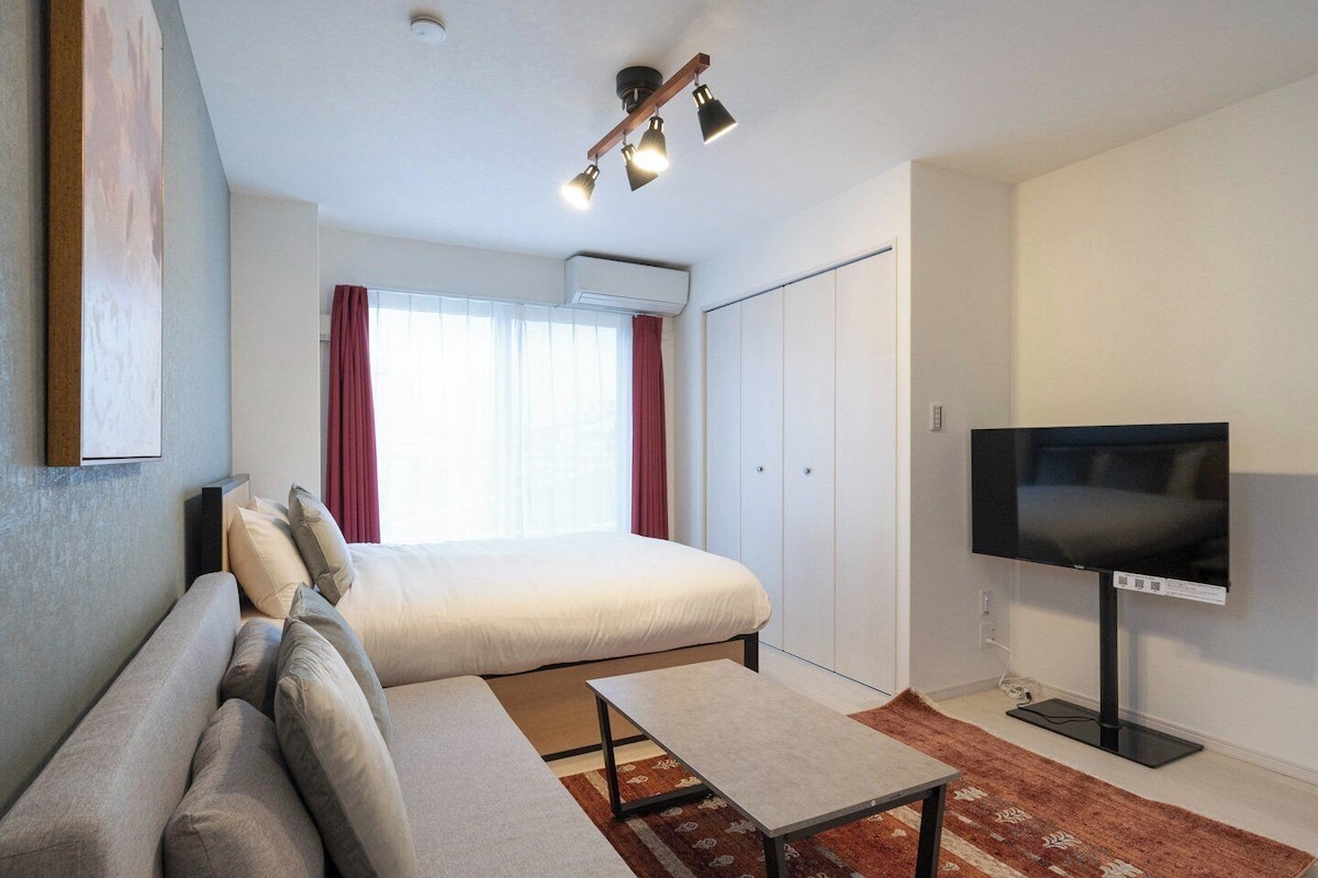 Quarto de hotel com cama, sofá, televisão e janela com cortinas.