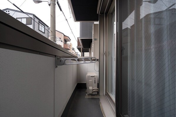 A narrow corridor with a window on the right, a door on the left, and a small air conditioning unit in the center. - Rufura Fukusima (Osaka)