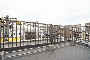 A rooftop terrace with a metal railing, a concrete floor, and a view of buildings and industrial structures. - Rufura Fukusima (Osaka)