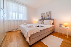 Un dormitorio con cama, lámparas de noche, mesita de noche y ventana con cortinas.