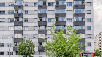 A multi-story residential building with balconies, a visible storefront, and a clear sky.