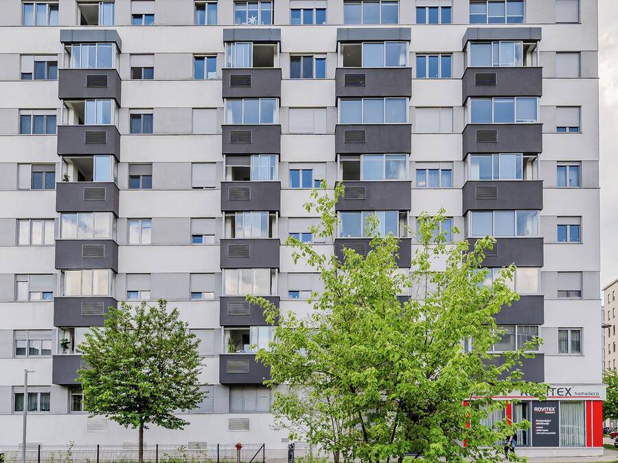 A multi-story residential building with balconies, a visible storefront, and a clear sky.