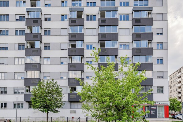 Un edificio residencial de varios pisos con balcones, una fachada comercial visible y un cielo despejado.