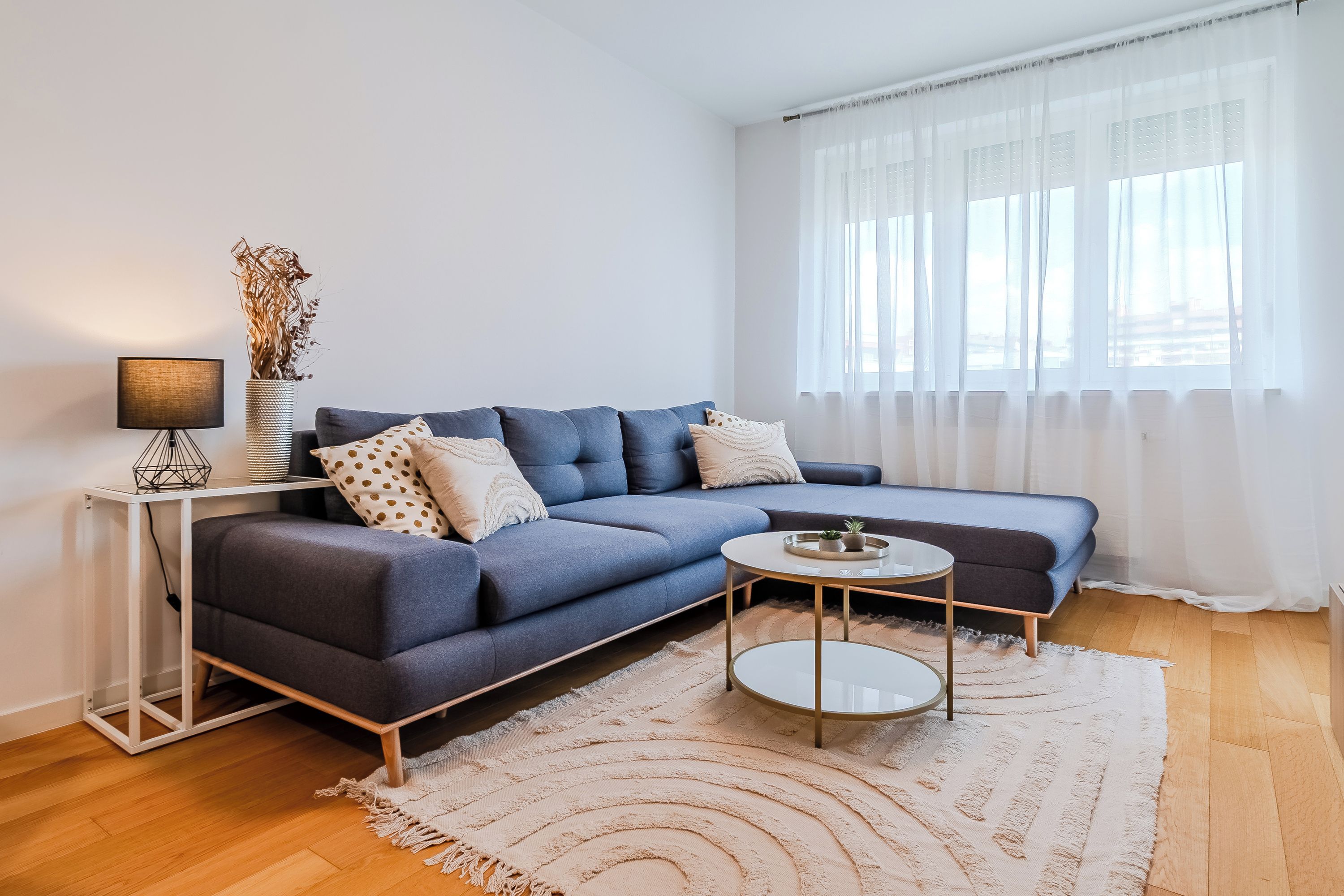 A modern living room with a sofa, a small round table, a lamp, and a vase with dried plants.