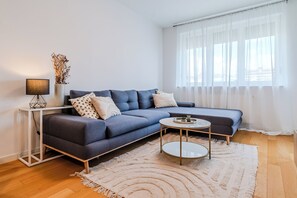 Una sala de estar moderna con un sofá, una mesita redonda pequeña, una lámpara y un jarrón con plantas secas.