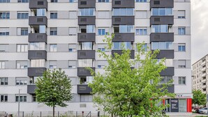 Un edificio residencial de varios pisos con balcones, una fachada comercial visible y un cielo despejado.