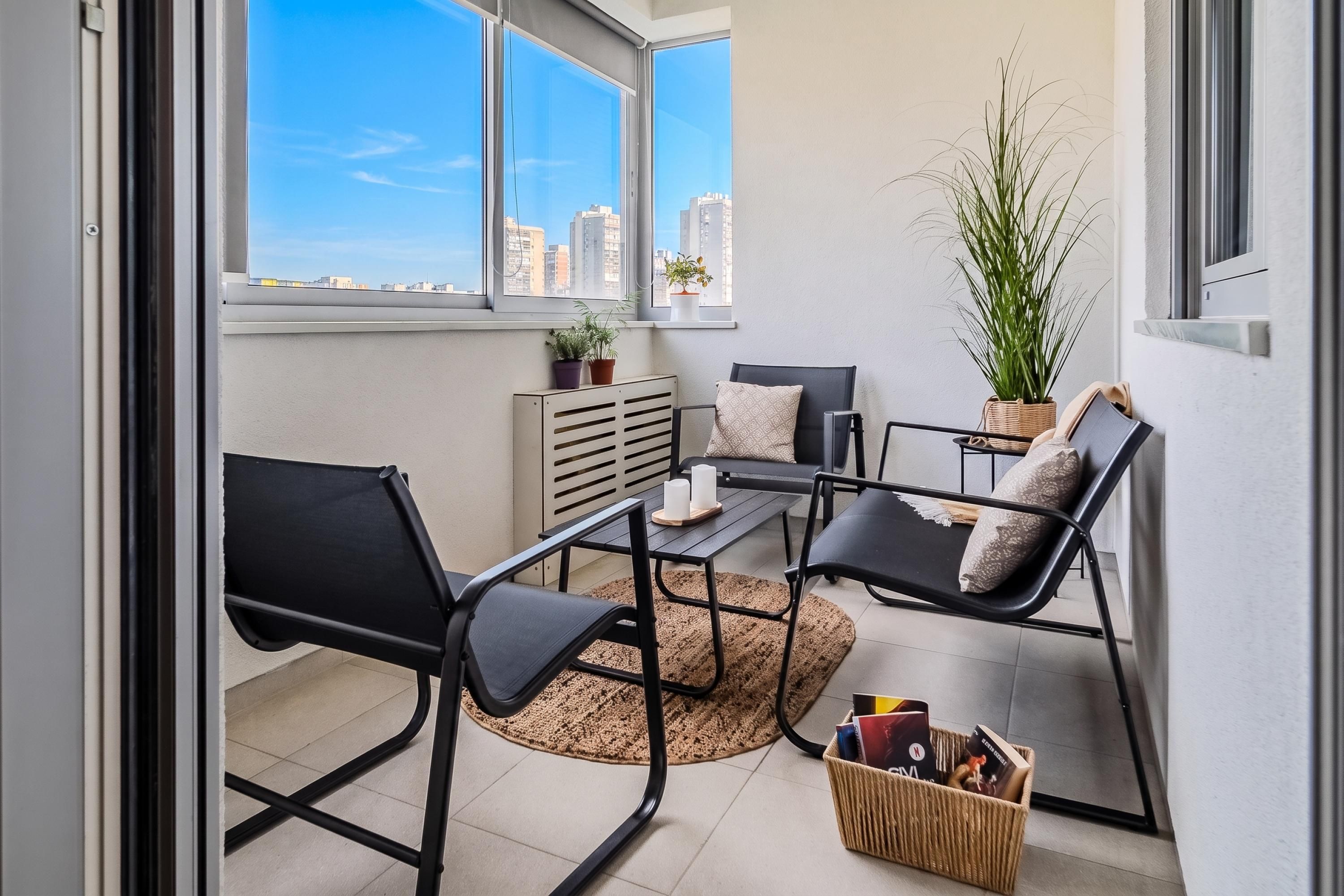 A balcony with a seating area, including two chairs and a table, a potted plant, and a small basket with items.