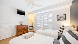 Et hotelværelse med to senge, en ventilator, et fjernsyn, en lampe og et billede på væggen.