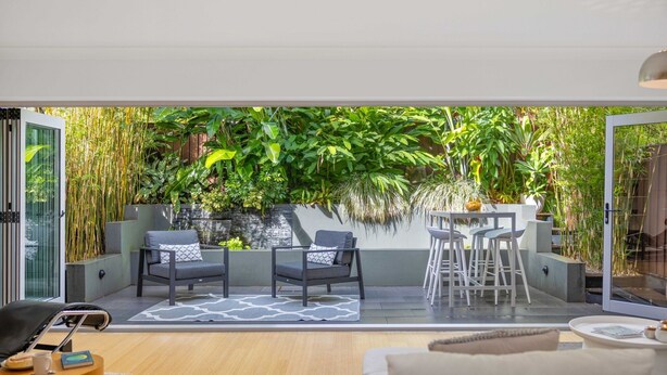 En moderne stue med en glasdør, der fører ud til en balkon med frodig beplantning.
