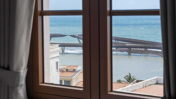 A window view of a coastal area with a bridge, buildings, and a clear sky. - Jenben Hotel (Phu Quoc)