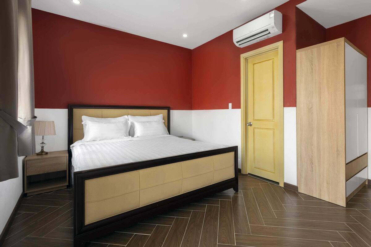 A bedroom with a bed, a nightstand, a wardrobe, and an air conditioning unit.
