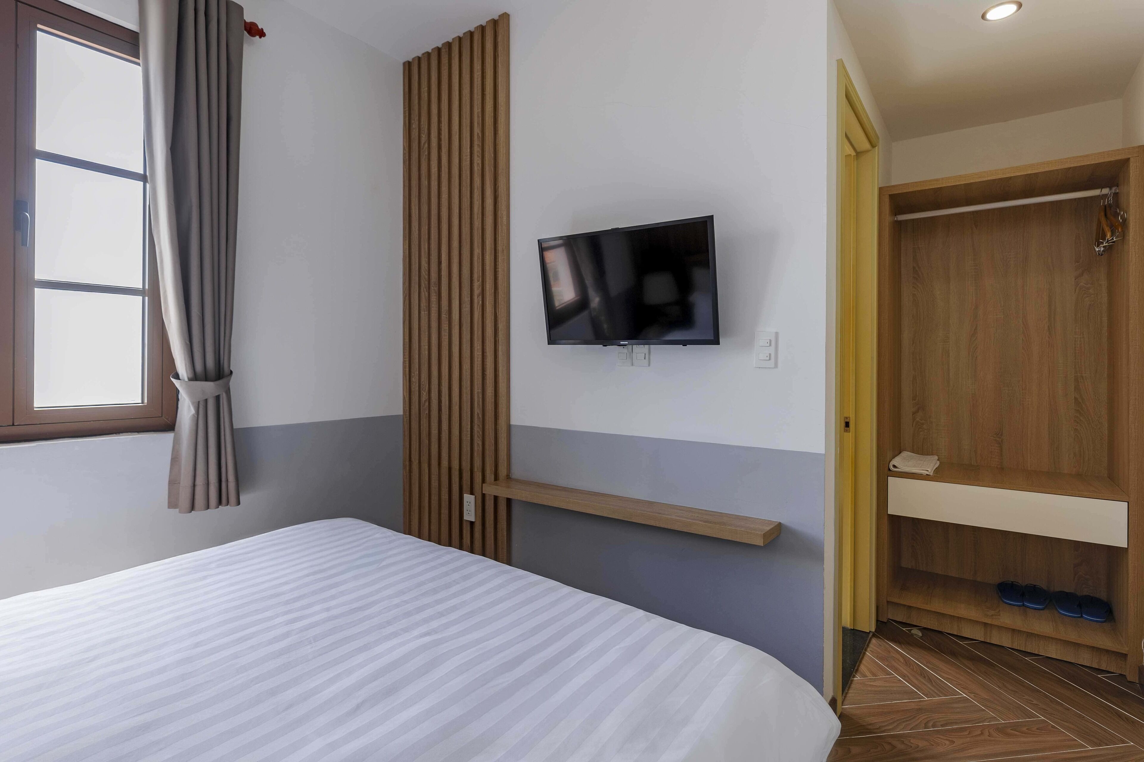 Ein Hotelzimmer mit einem Bett, einem an der Wand montierten Fernseher, einem Holzschrank und einem Schuhregal.