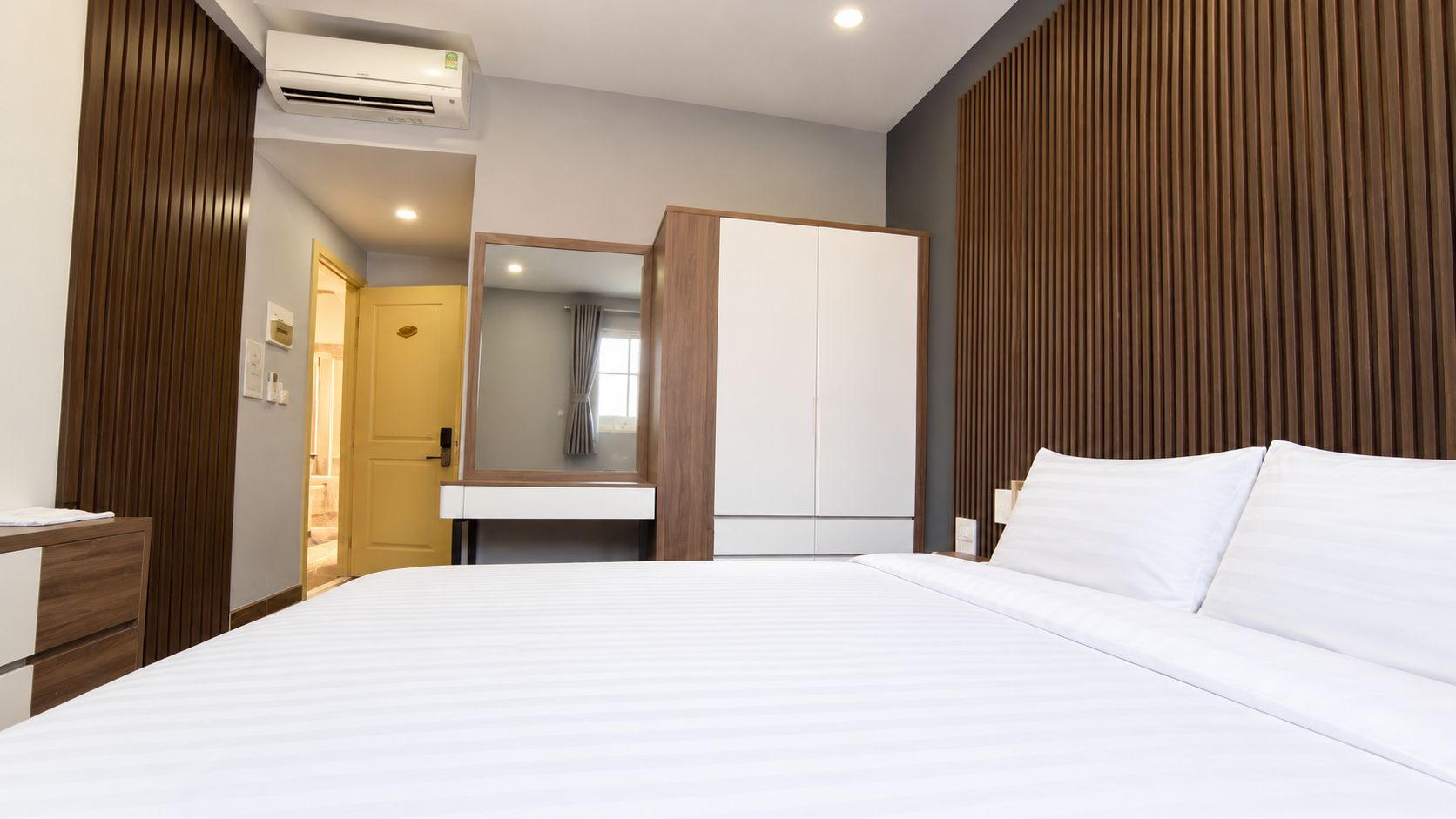 A hotel room with a bed, a wardrobe, a mirror, and an air conditioning unit.