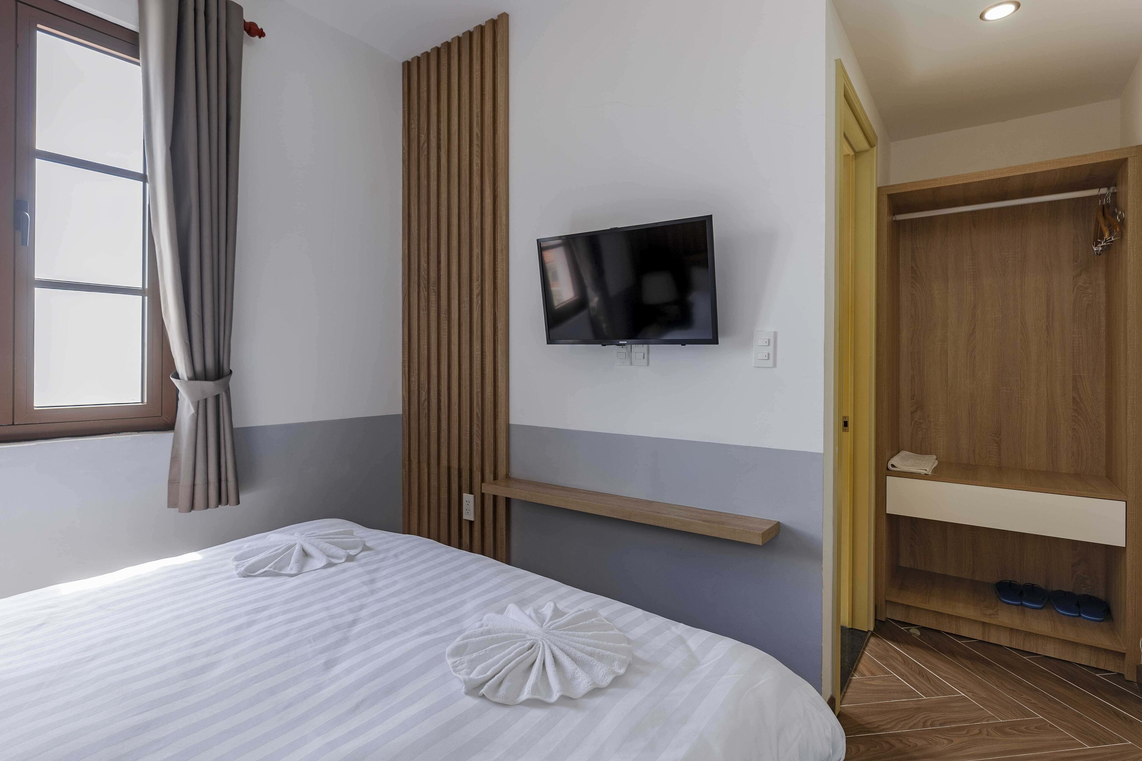 Una camera d'albergo con un letto, una TV a muro, un armadio in legno e un portascarpe.