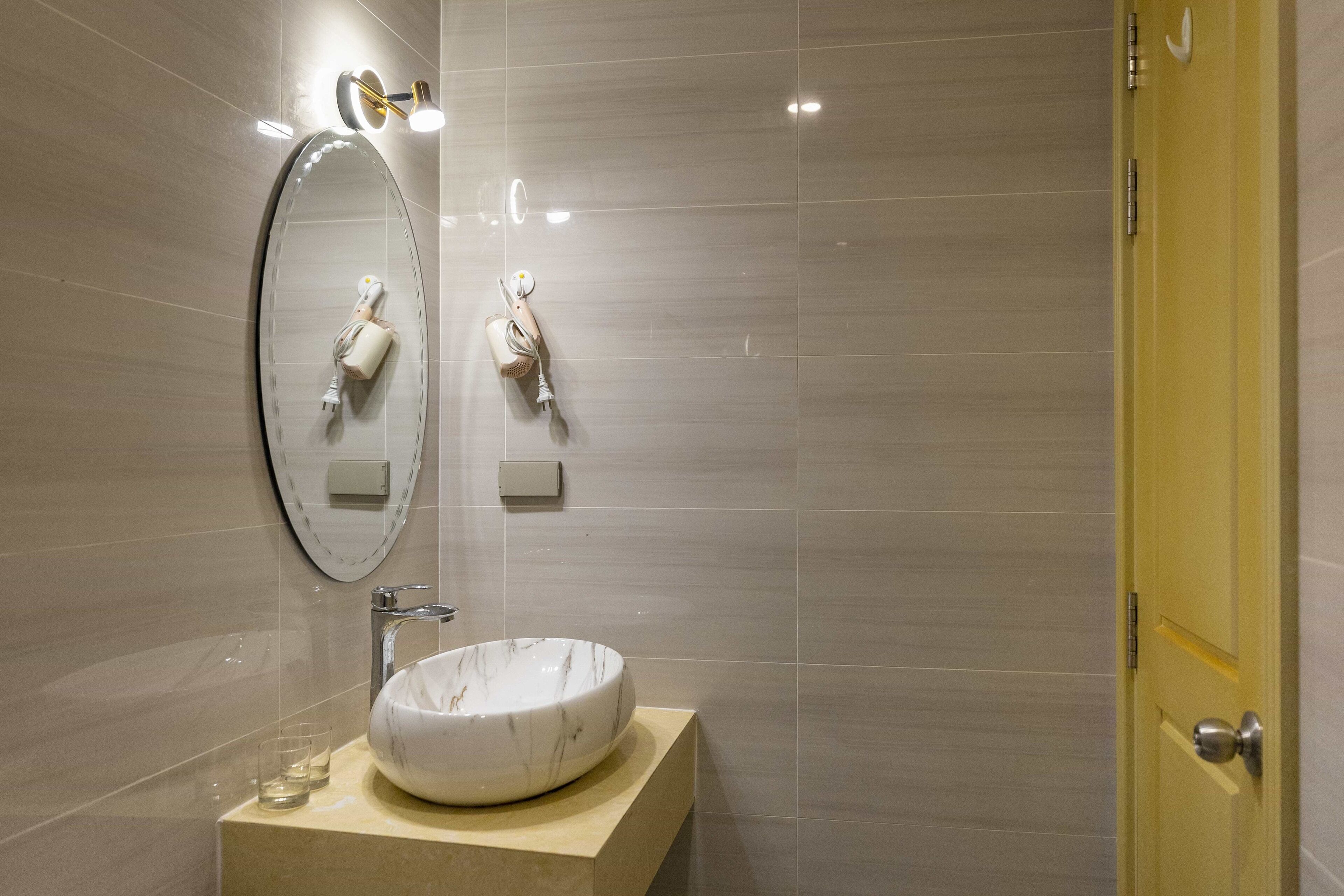 A bathroom with a round marble sink, a mirror, and two towel dispensers.