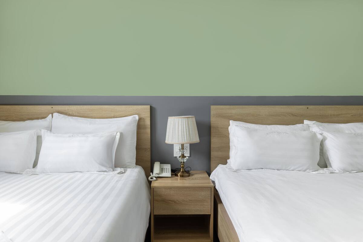 A hotel room with two beds, a nightstand with a lamp, and a telephone.