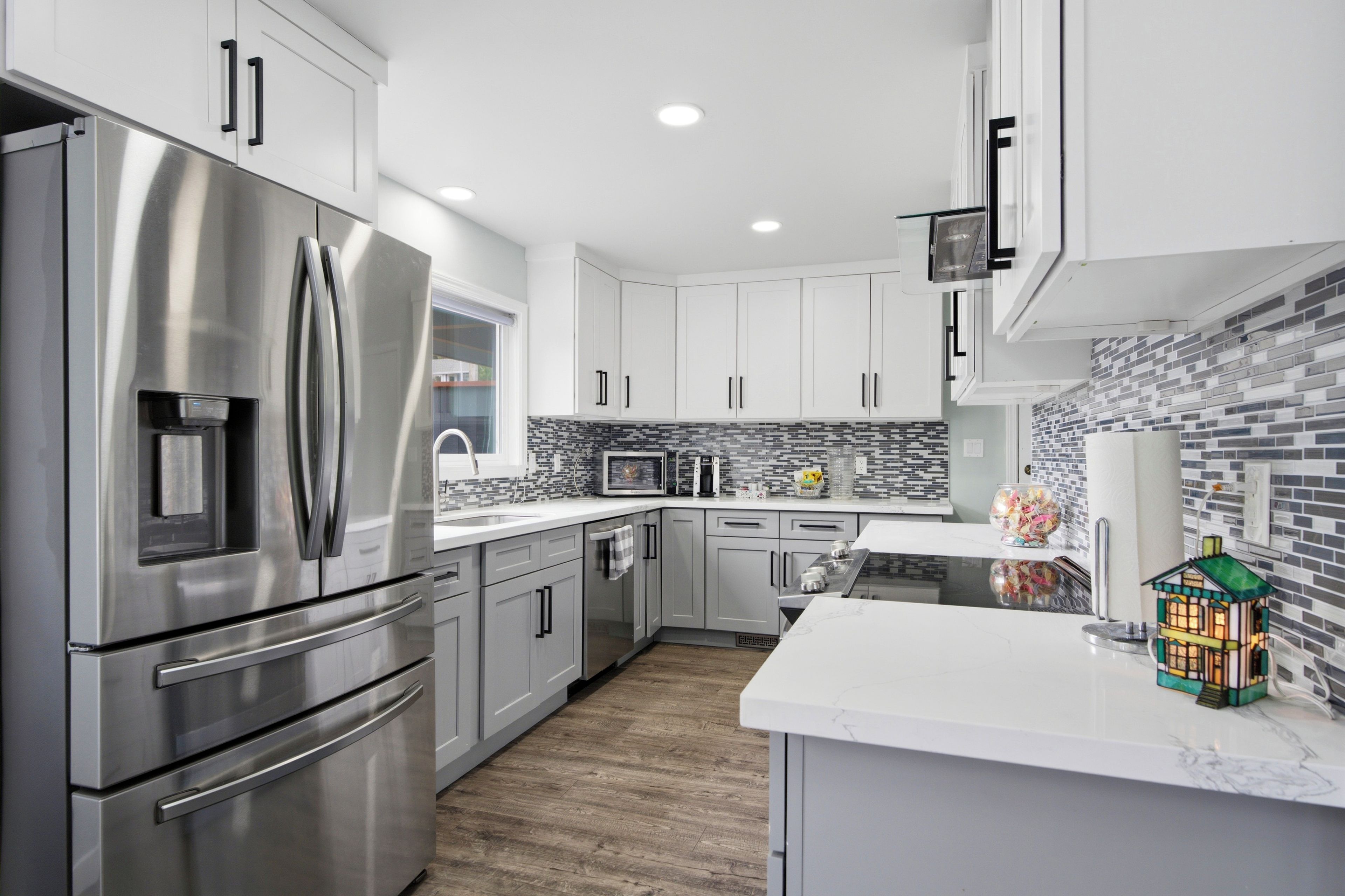 A modern kitchen with stainless steel appliances, white cabinetry, and a tiled backsplash.
