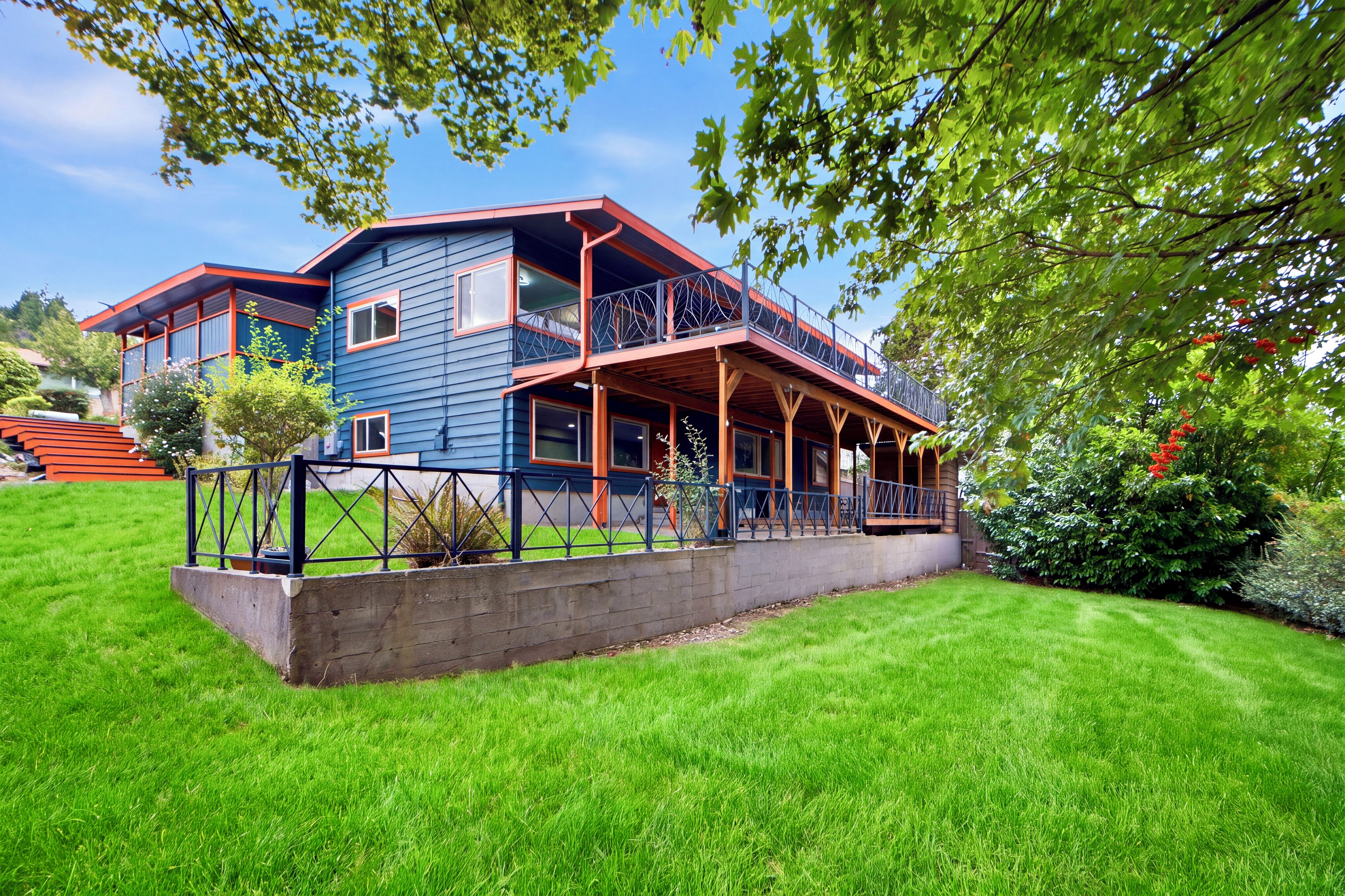 A two-story house with a balcony, surrounded by a well-maintained lawn and trees.
