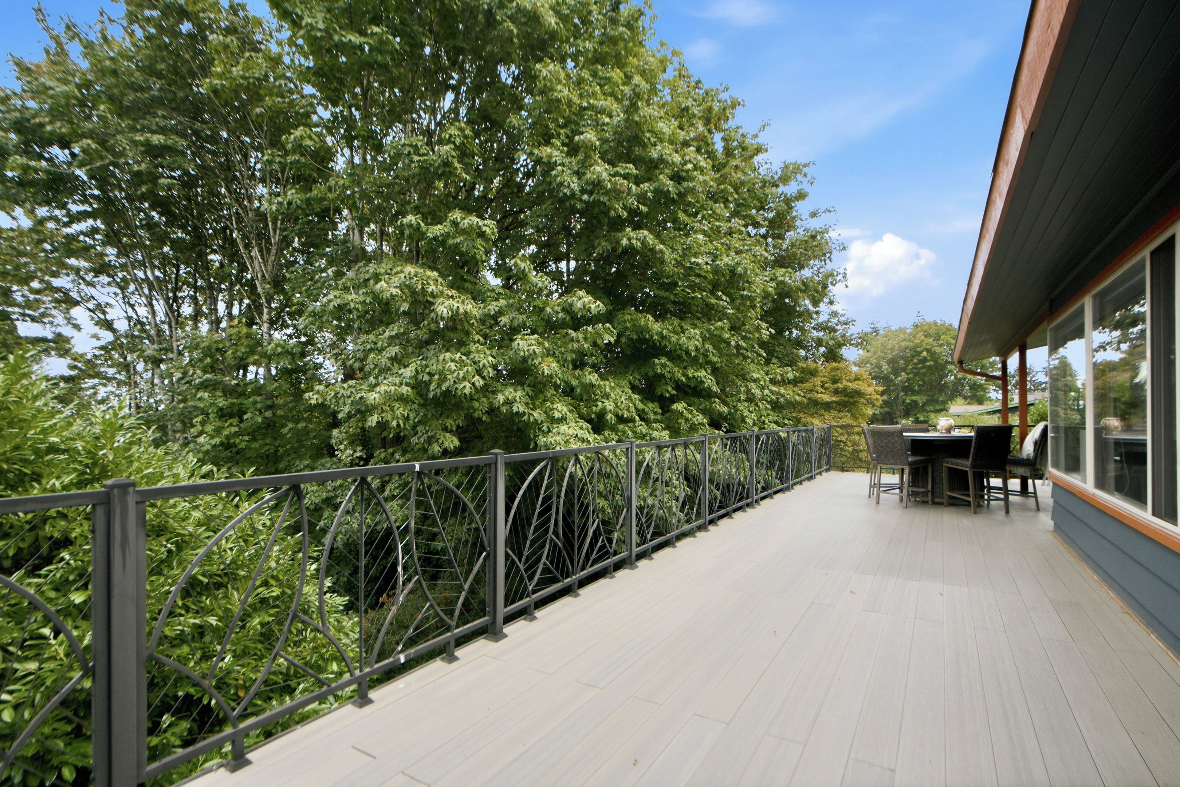 A deck with a metal railing, a table, and chairs, surrounded by dense foliage.