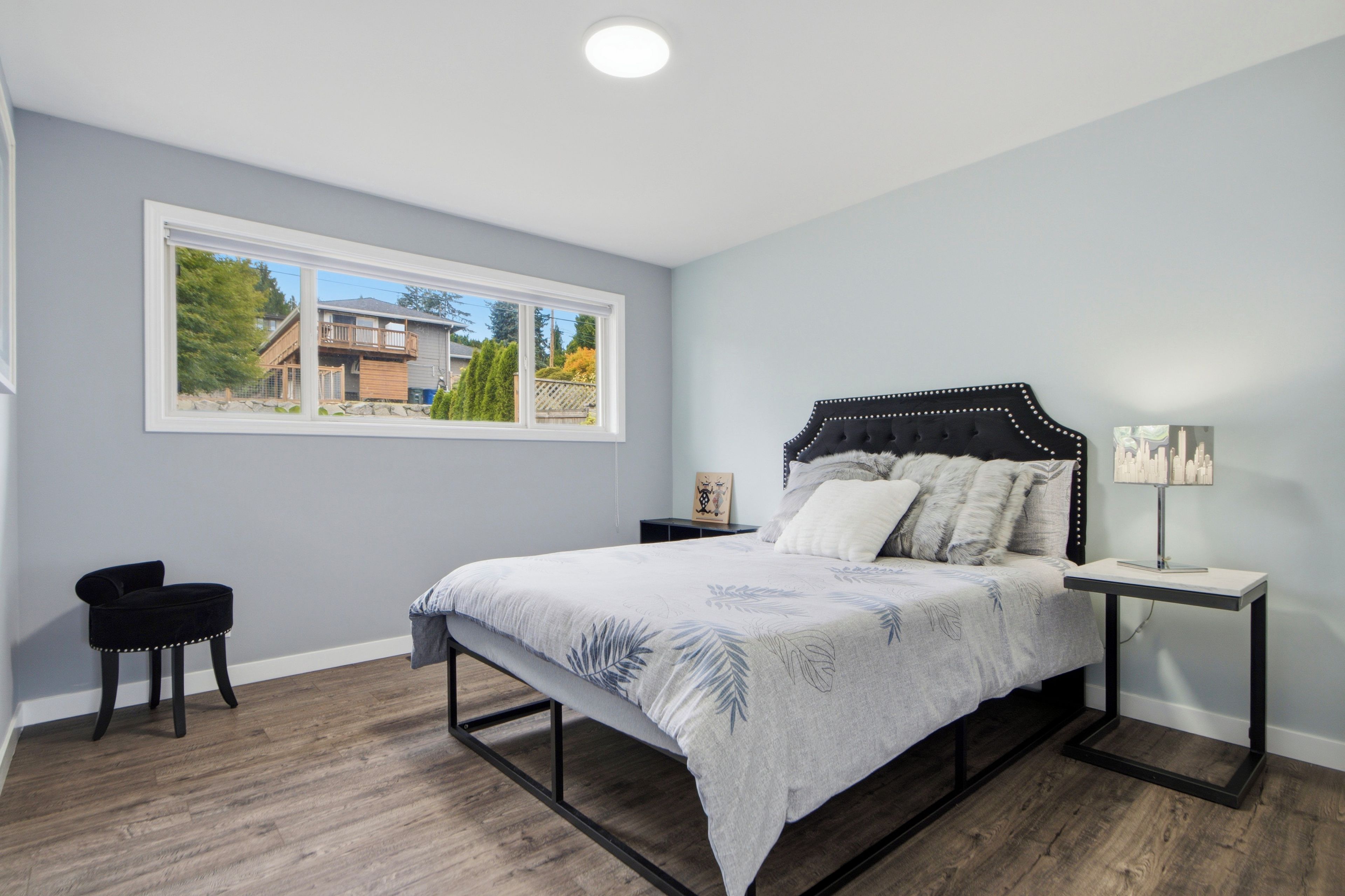 A bedroom with a bed, a nightstand, a chair, and a window with a view of a house and trees.