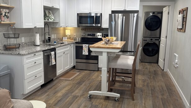 Une cuisine moderne avec des meubles blancs, des appareils en acier inoxydable, une table à manger en bois, ainsi qu’un lave-linge et un sèche-linge intégrés.