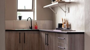 A kitchen with wooden cabinets, a black faucet, a window, and a shelf with kitchen items. - Chalo villa's and farm (Chitedze)