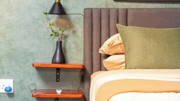 A bedroom with a bed, a bedside table with a lamp, a wall outlet, and a framed artwork.