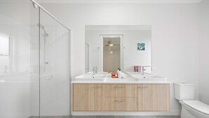 Et moderne badeværelse med en glasbrusekabine, to håndvaske, et toilet og en trækommode.