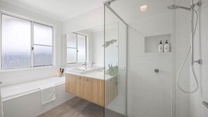 Et moderne badeværelse med en glasafskærmet bruseniche, et stort spejl, et badekar og en vaskepult med vask.