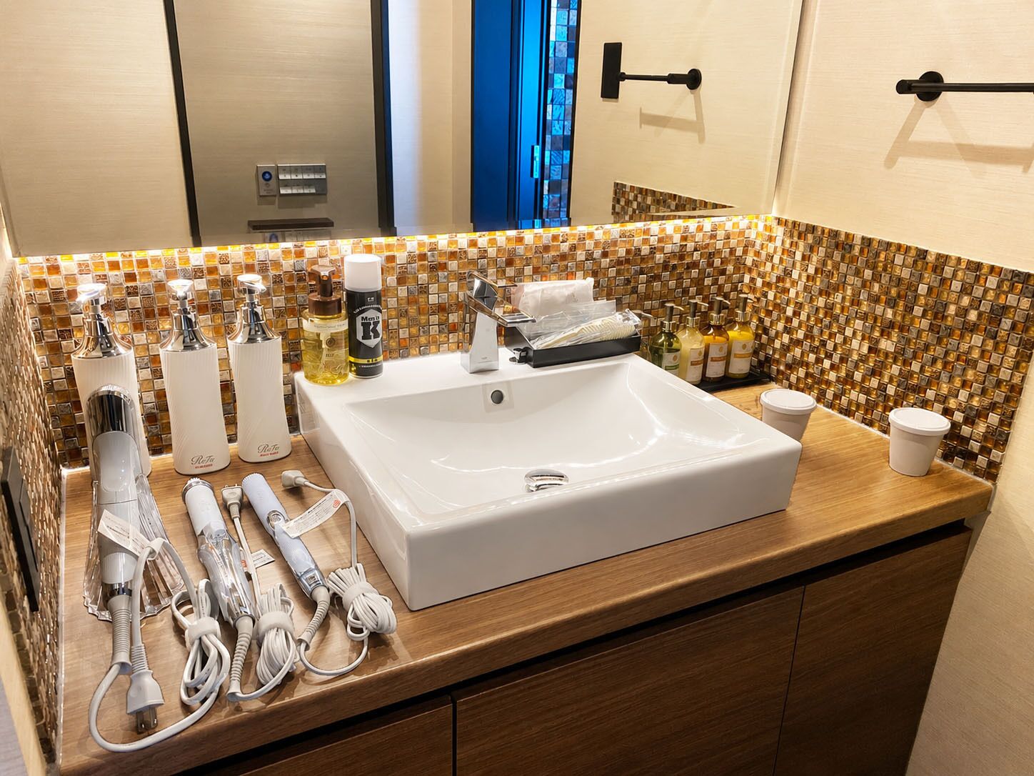 A hotel bathroom with a large white sink, multiple toiletries, and a mirror.