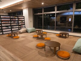 Interior moderno de biblioteca con estanterías, zonas de descanso y grandes ventanales.