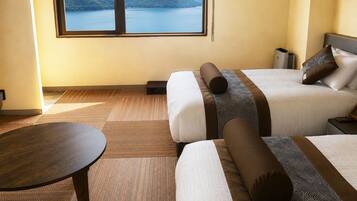 A hotel room with two beds, a view of a lake and mountains, a round table, and a small bedside table.
