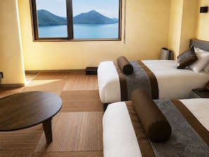 A hotel room with two beds, a view of a lake and mountains, a round table, and a small bedside table. - Livemax Resort Mihara Sea Front (Mihara)