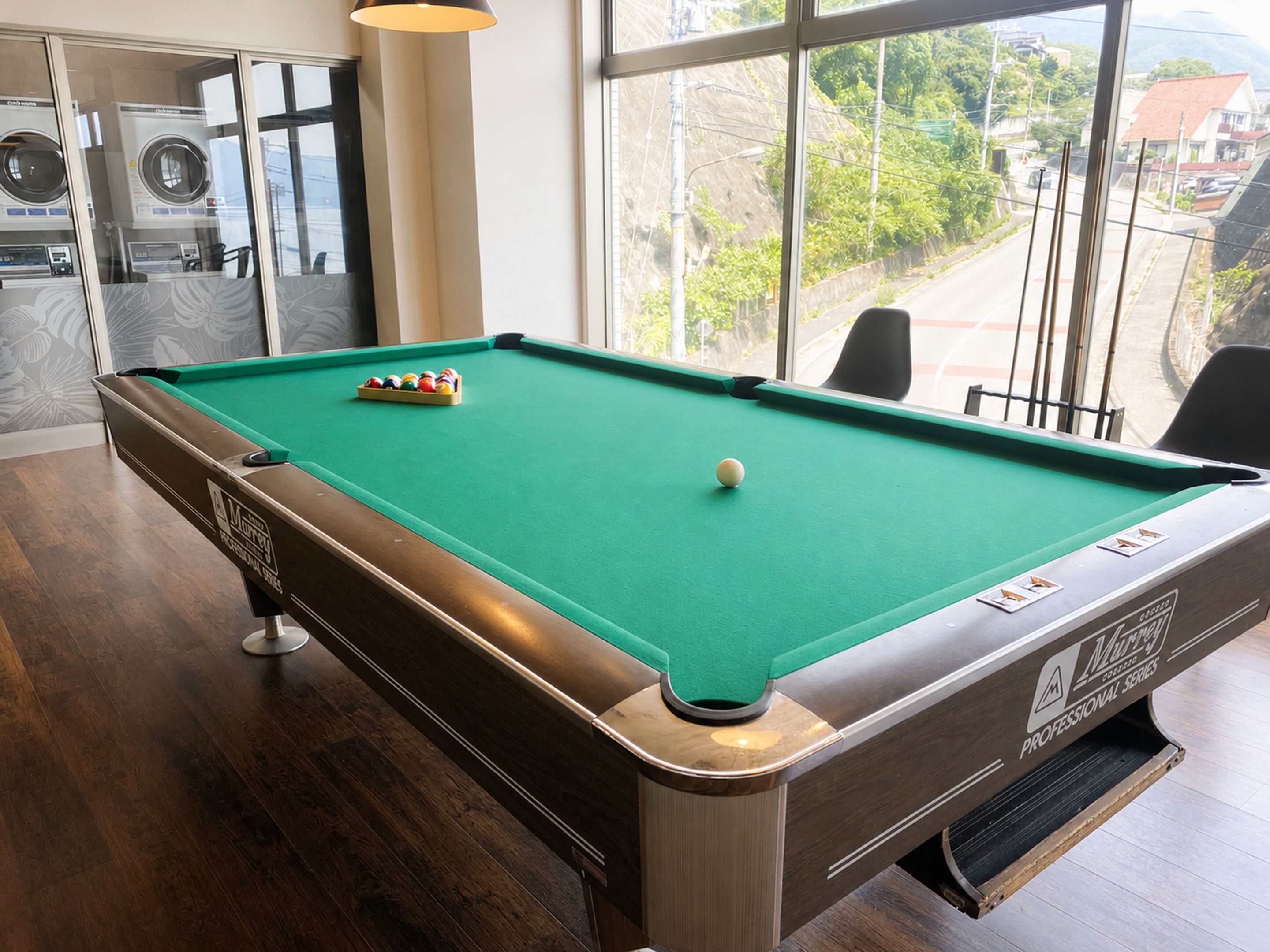 Una mesa de billar con superficie de fieltro verde, una bola blanca y un juego de bolas de colores en el centro.