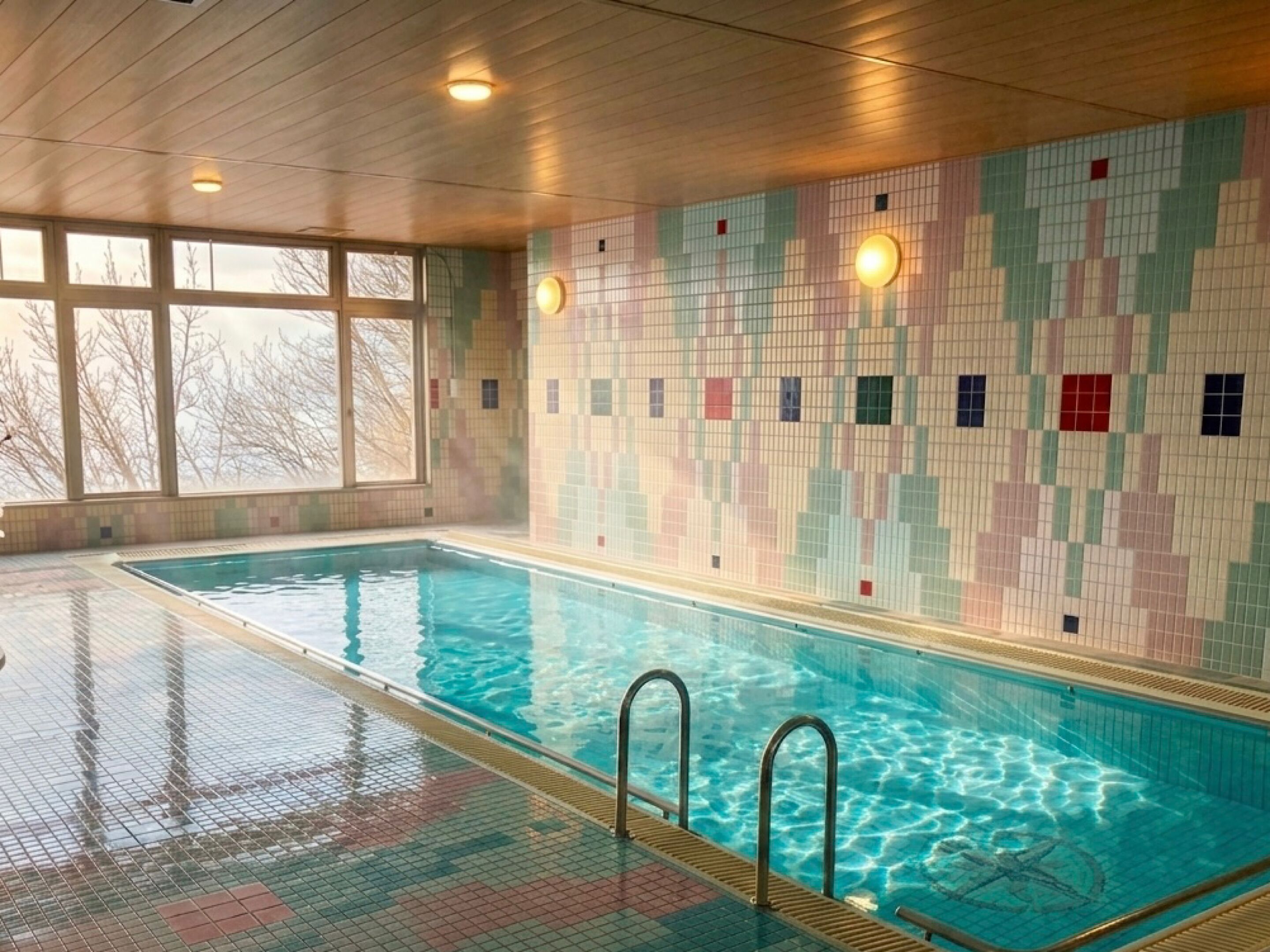 An indoor swimming pool with clear water, tiled walls, and a wooden ceiling.