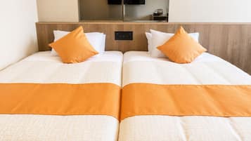 Habitación de hotel con dos camas, cada una con ropa de cama blanca y detalles en naranja, un televisor de pantalla plana en la pared y un cabecero de madera.