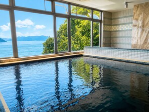 An indoor swimming pool with clear windows offering a view of a body of water and greenery. - Livemax Resort Mihara Sea Front (Mihara)