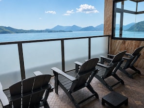 A balcony with chairs and a table overlooking a lake with mountains in the distance. - Livemax Resort Mihara Sea Front (Mihara)