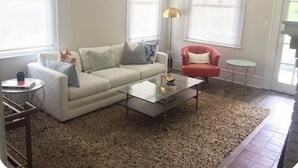 Ein Wohnzimmer mit einem weißen Sofa, einem roten Sessel, einem Glastisch und einem beigen Teppich.