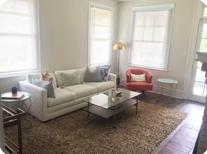 Ein Wohnzimmer mit einem weißen Sofa, einem roten Sessel, einem Glastisch und einem beigen Teppich.