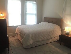 A bedroom with a bed, a nightstand with a lamp, a dresser, and a window with blinds. - Top floor of 1920’s duplex in the cool & eclectic 5-points Riverside area (Jacksonville)