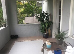 Ein Balkon mit einem Blumentopf, einem kleinen Tisch mit Dekoration und Blick auf ein Haus und Bäume.
