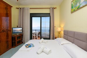 Une chambre dâhĂŽtel avec un lit, une tĂ©lĂ©vision, une vue sur la mer et un balcon Ă©quipĂ© de chaises.