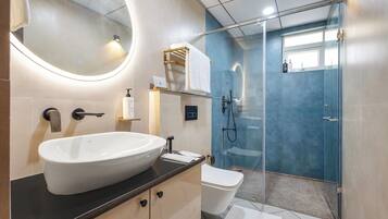 A modern bathroom with a large oval sink, a toilet, a glass-enclosed shower, and a mirror with a circular light.