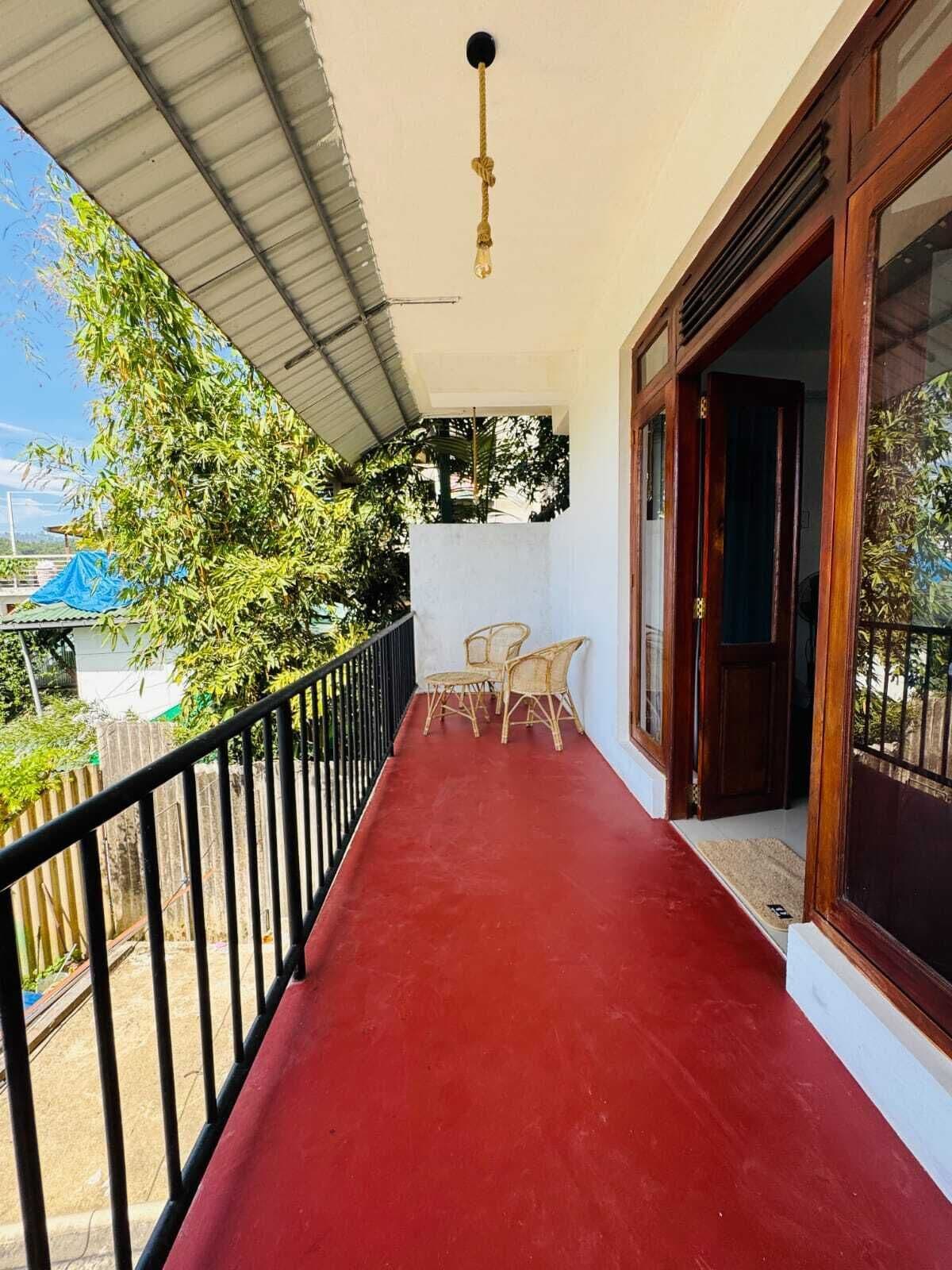 Ein Balkon mit rotem Boden, schwarzem Geländer und zwei Korbstühlen.