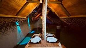 An interior with a wooden table set for two, a thatched roof, and a wooden beam structure. - Nest of peak  (Ella)