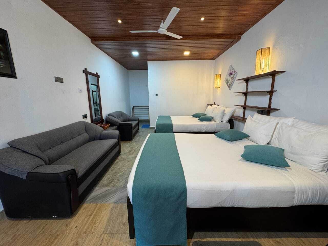 Camera d'albergo con due letti, un divano, una ventola a soffitto e lampade a parete.